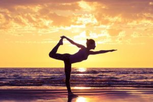 Frau macht Yoga am Strand bei Sonnenuntergang